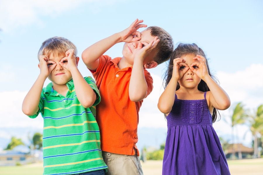 Three kids make silly faces outdoors on a sunny day.
