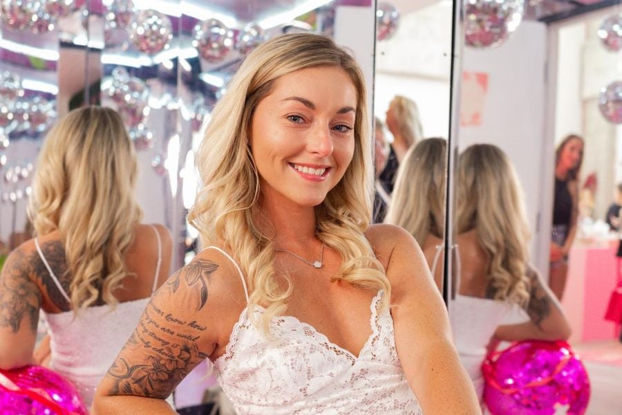 A smiling woman in a white lace dress poses in front of mirrors and disco balls.