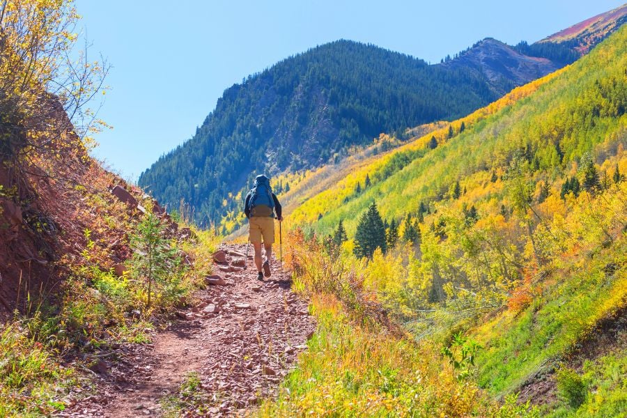 A hiker climbs a rocky trail framed by colorful autumn hills.