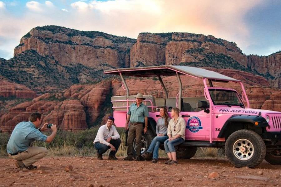 People are posing for a photo next to a pink jeep in front of red rocks.