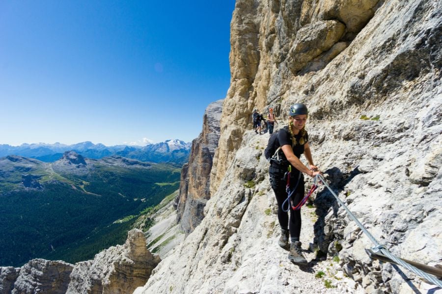 Adventurers climbing a steep mountain trail with safety ropes and helmets.