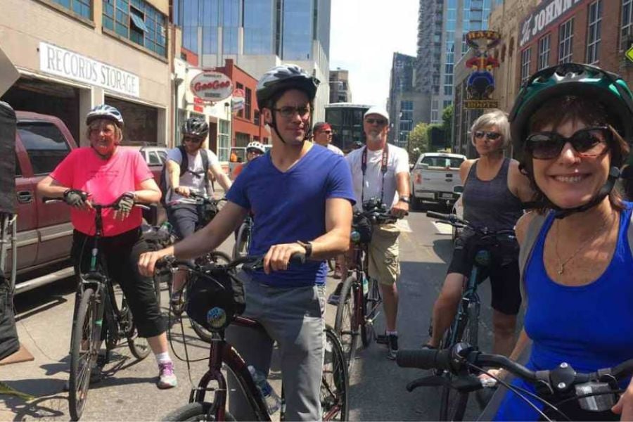 Smiling riders enjoy a sunny day bike tour through a bustling city street.