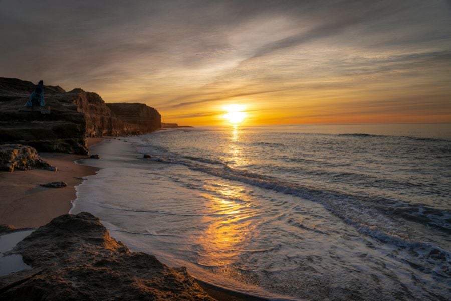 Peaceful sunset over a rocky beach with waves washing onto the sand.