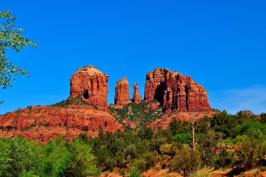Tall red rock towers rise under a bright blue sky in Sedona.