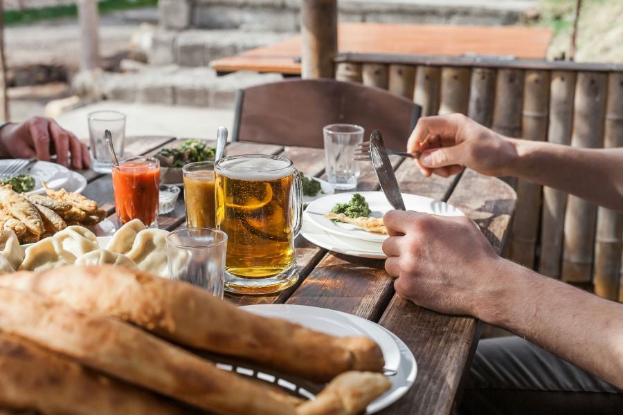 A rustic outdoor meal with beer, bread, and plates of homemade food.