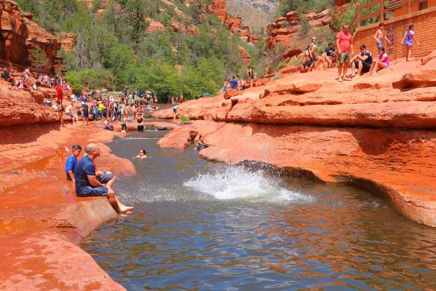 People swim and splash in a natural red rock water slide.