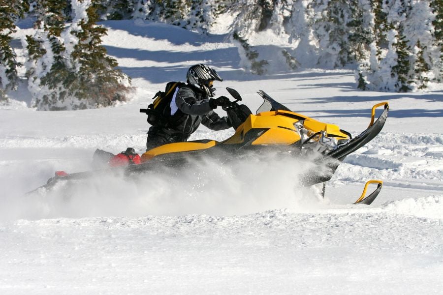 A rider speeds through fresh Breckenridge snow on a powerful yellow snowmobile.