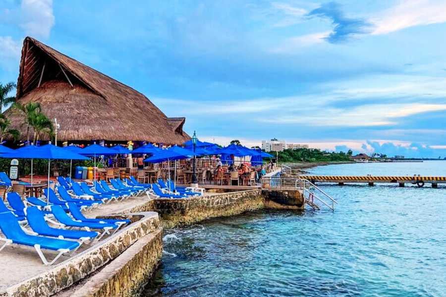 A row of blue lounge chairs lines the waterfront, offering a perfect spot to unwind by the crystal-clear sea.