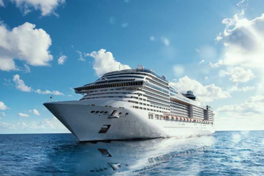 A massive cruise ship sailing through the ocean, with vibrant blue skies and fluffy clouds above.