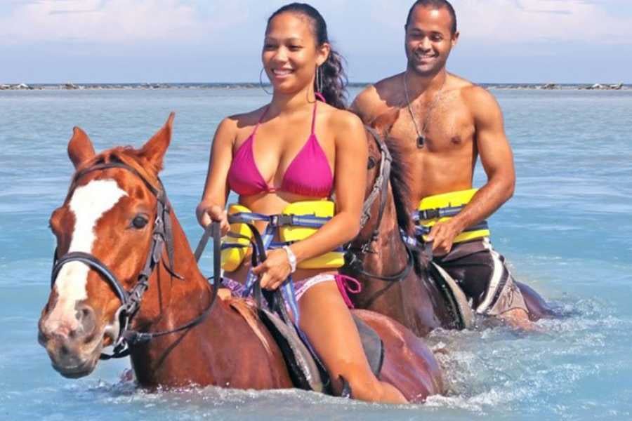 Two riders on horseback enjoy a refreshing swim in the Caribbean Sea.