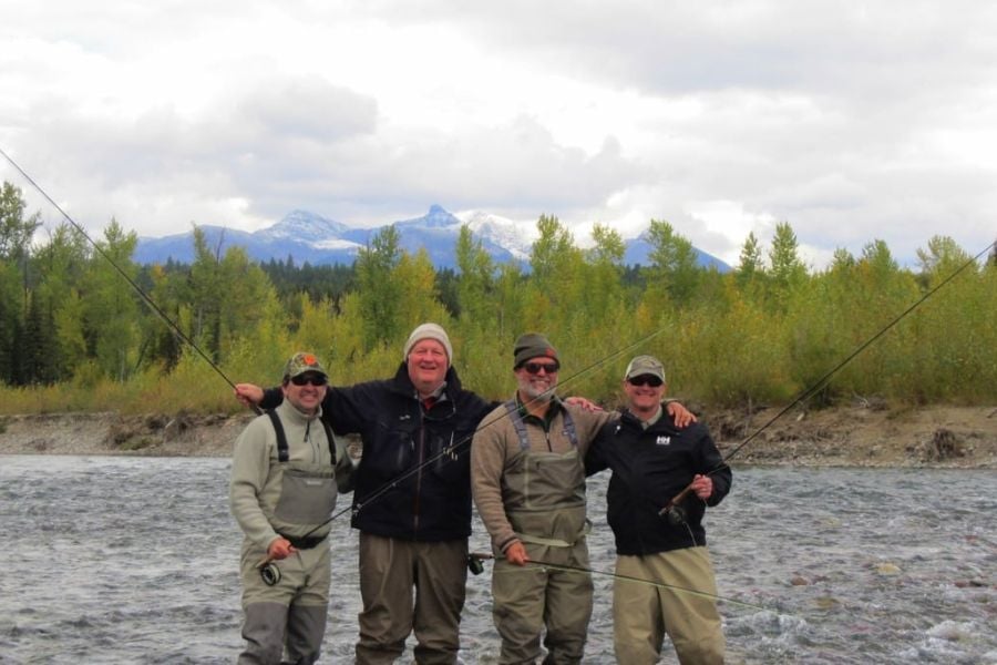 Four friends posing together on the riverbank, fishing rods in hand and smiles all around.