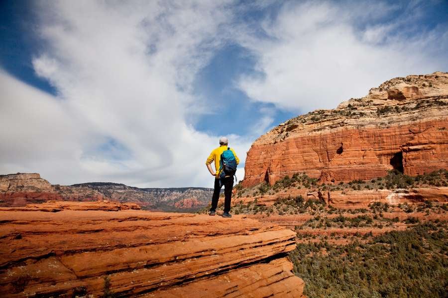 A man in yellow stands on a cliff, admiring the red rock canyon views.