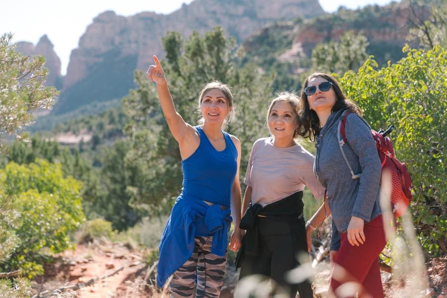 Three friends explore a scenic trail, pointing at the stunning red rock formations ahead.