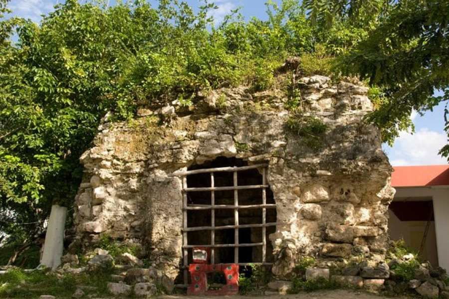 An ancient stone structure with a gated entrance, partially covered in greenery, standing as a mysterious historical site.