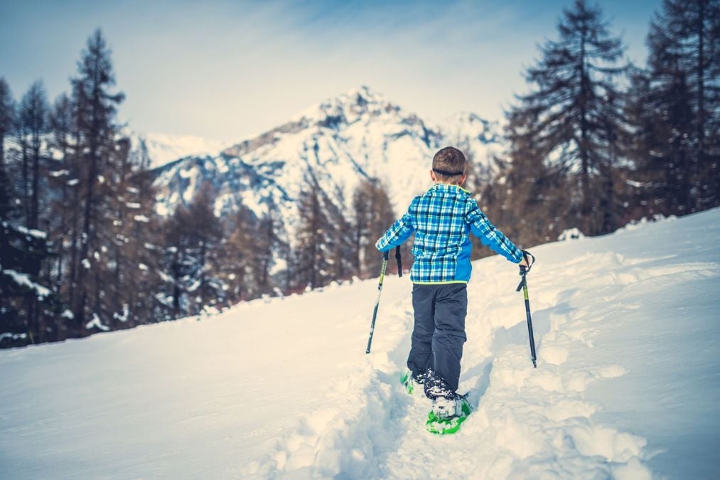 A child snowshoes along a snowy Breckenridge trail with tall peaks behind him.