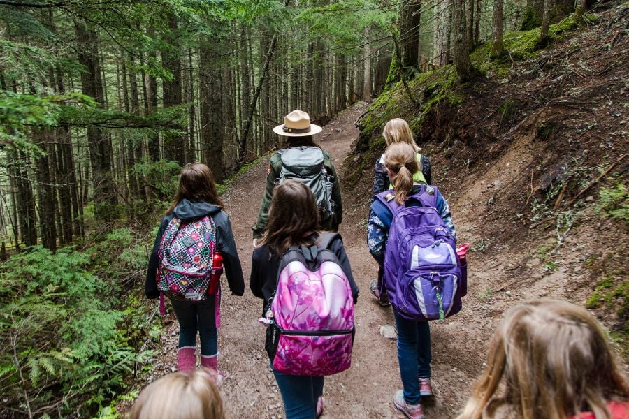 A ranger leads a group of kids hiking through a lush forest.