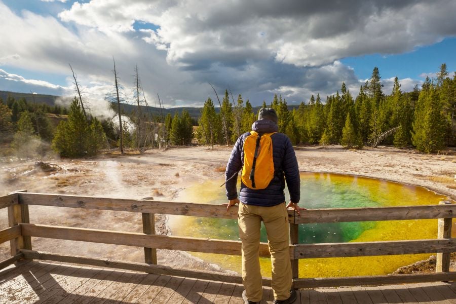 Traveler admiring a colorful hot spring in Yellowstone.