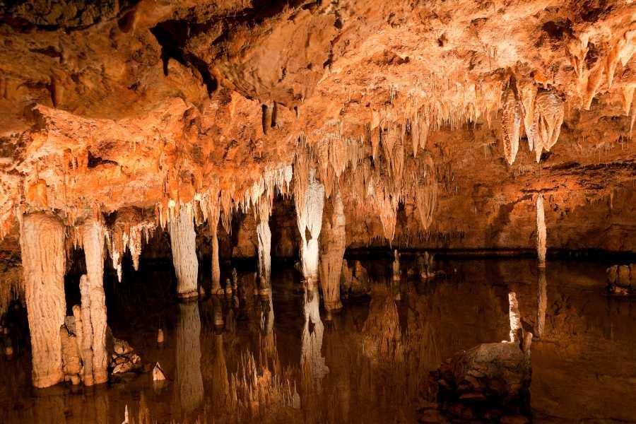 Stalactites and stalagmites create a mesmerizing underground world, their reflections dancing on the water's surface.