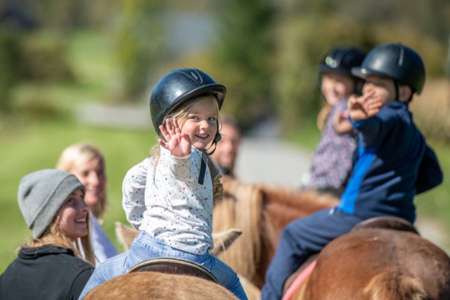 Kids smile and wave while horseback riding on a sunny Breckenridge trail.