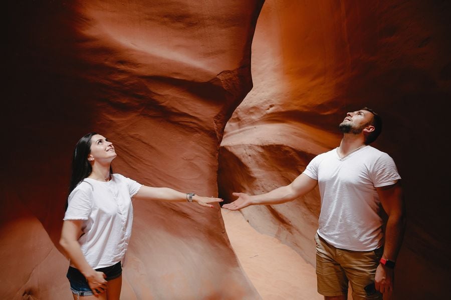 A couple explores a narrow, red rock canyon with smooth, curvy walls in Sedona.