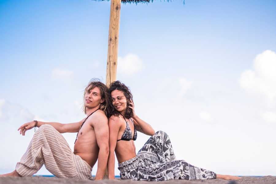 A couple relaxes on the sand under a shaded hut.