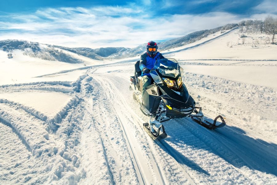 A snowmobiler cruises Breckenridge&rsquo;s open trails with snowy hills in the distance.