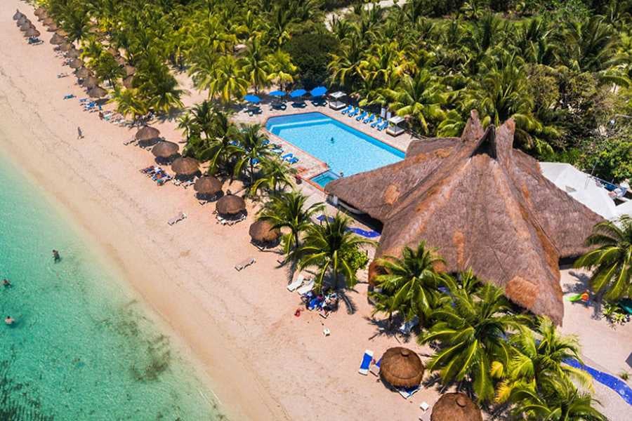 A stunning aerial view of a beachside resort with a pool, thatched-roof cabanas, and turquoise waters in the background.