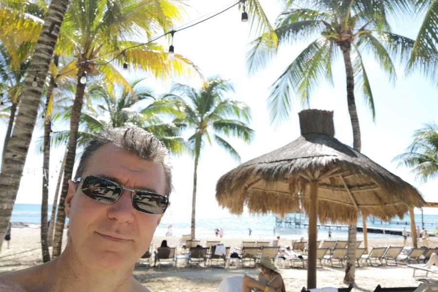 A selfie against a backdrop of palm trees and a serene beach under the bright sunlight.