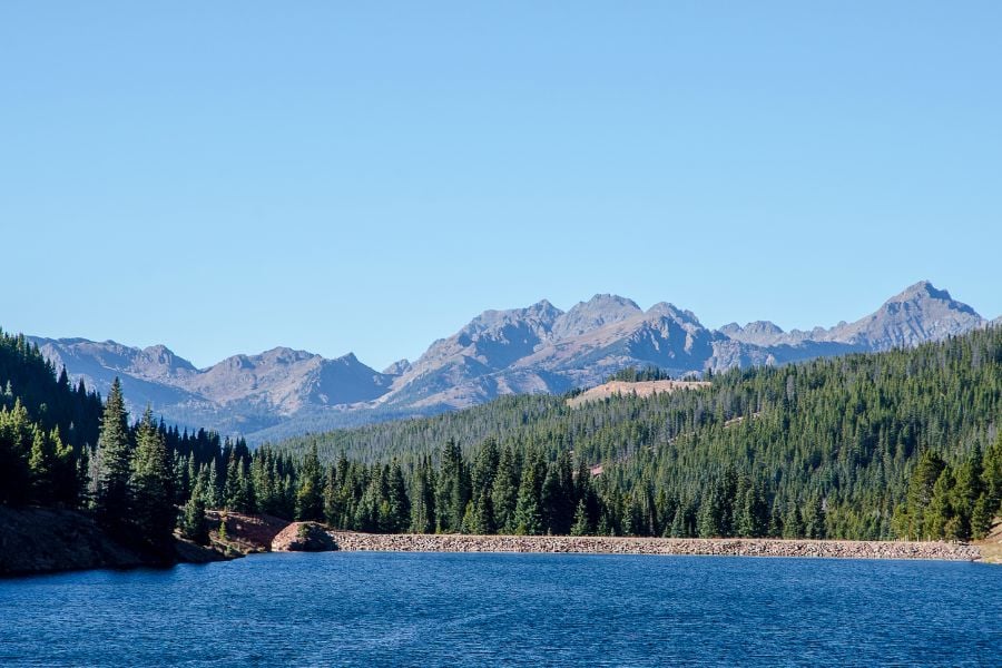 A blue mountain lake sits below jagged peaks and endless pine forests.