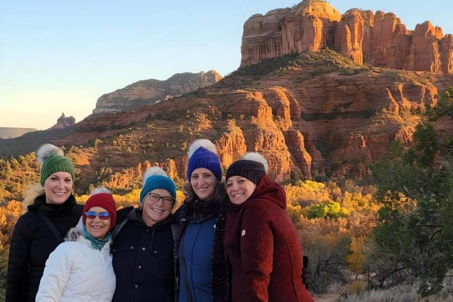 A happy group smiles with red rocks glowing in the sunset behind them.
