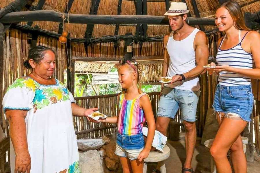 A family enjoys an authentic Mayan experience, sharing traditional food with a welcoming host in a rustic setting.