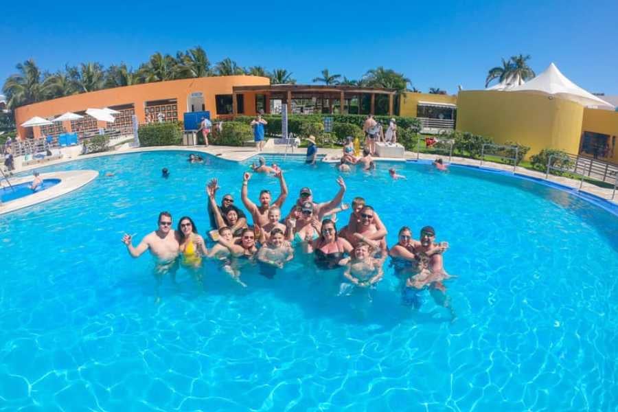 A group of happy vacationers enjoy the sun, cooling off in a bright blue resort pool.