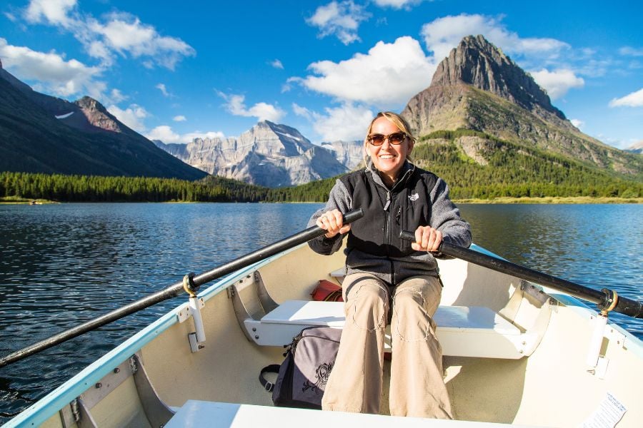 A woman rows a small boat on a clear mountain lake under sunny skies.