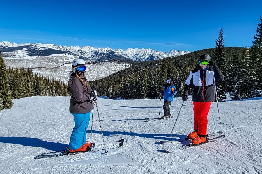 Friends pause mid-slope, admiring the snowy mountains under a bright blue sky.