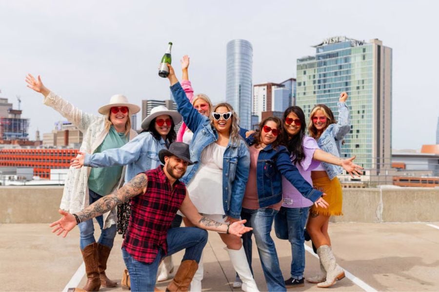Friends in denim and boots celebrate on a rooftop with city views and champagne fun.