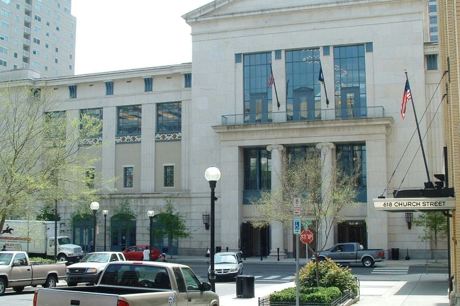 A grand stone building with tall windows stands in the middle of the city.