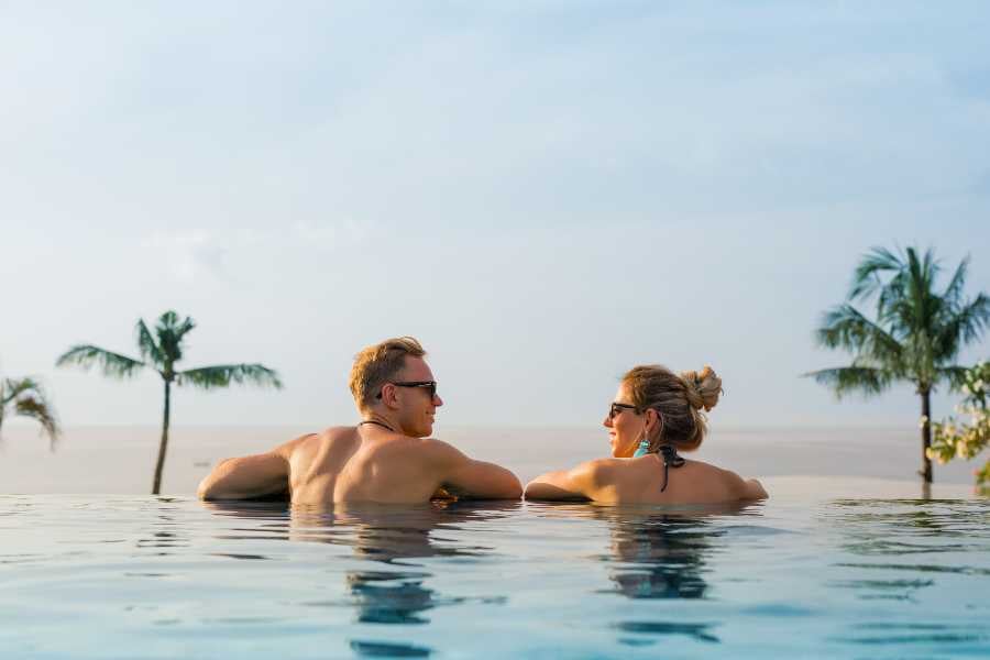 A couple relaxes in an infinity pool, enjoying the view of the ocean and palm trees.