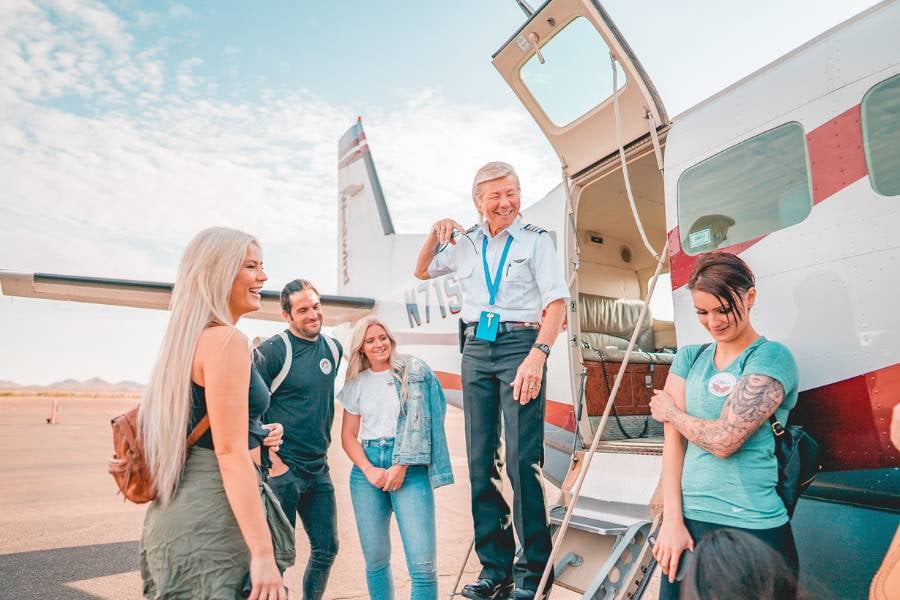 A friendly pilot talks to passengers getting ready to board a small airplane.