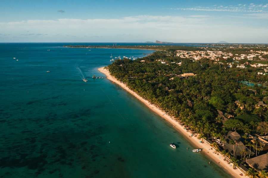 A stunning aerial view of a coastline with lush greenery and boats in the clear, inviting waters.