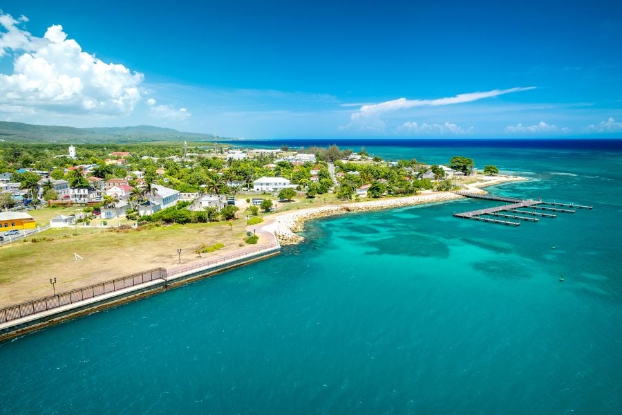 A bright aerial view of Falmouth’s coastline with turquoise water and small homes.