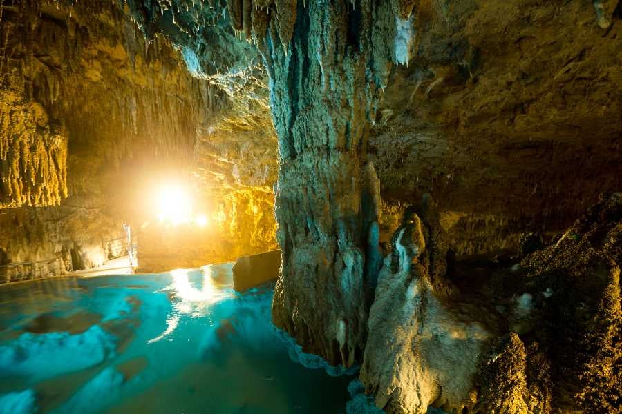 A golden-lit cave reflects off its still, clear waters, showcasing towering rock structures and glowing textures.