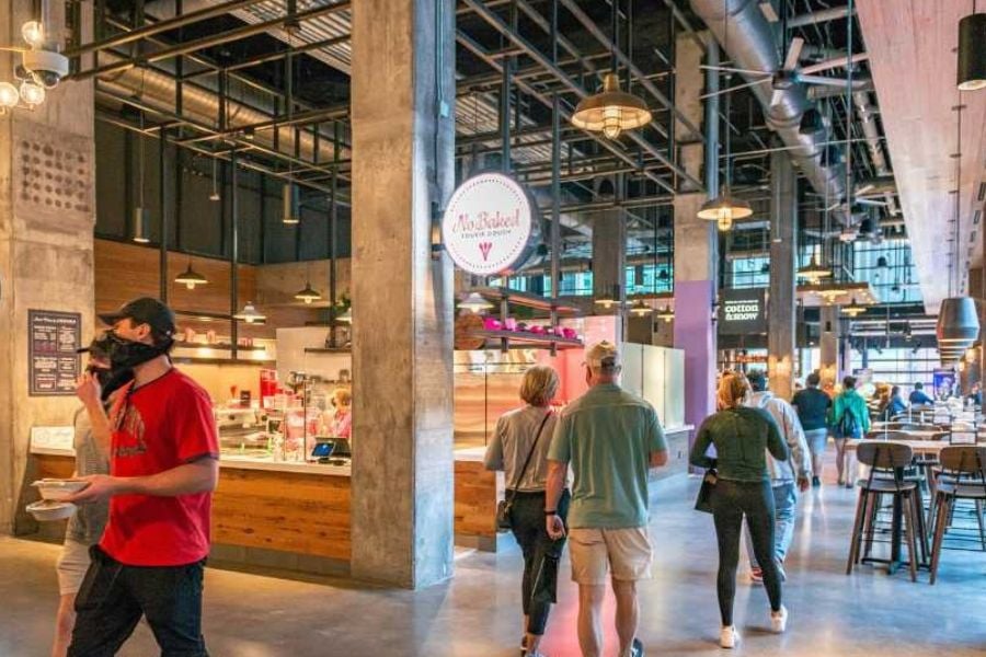 People walk through a bright and busy indoor food hall.