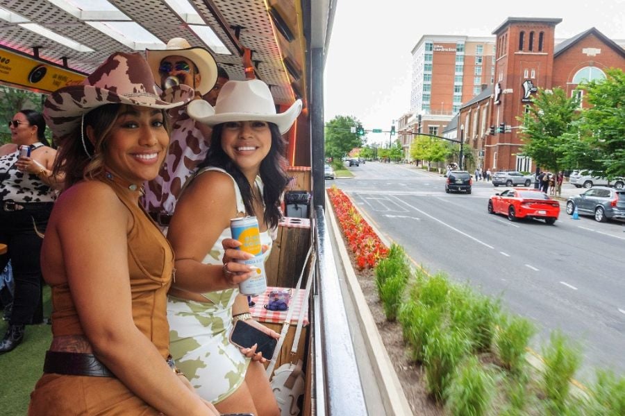 Two women in cowboy hats enjoy drinks on a lively ride through the city.