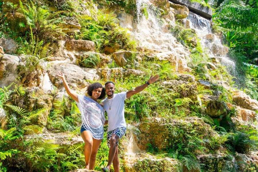 A couple enjoys the beauty of a cascading waterfall, surrounded by lush greenery in a tropical paradise.