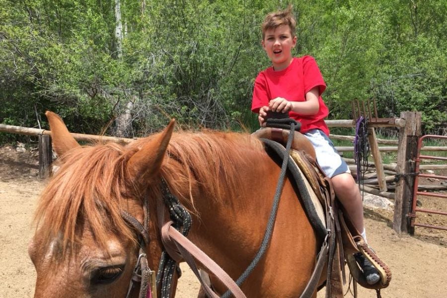 A boy experiences horseback riding near rustic corrals in Vail.