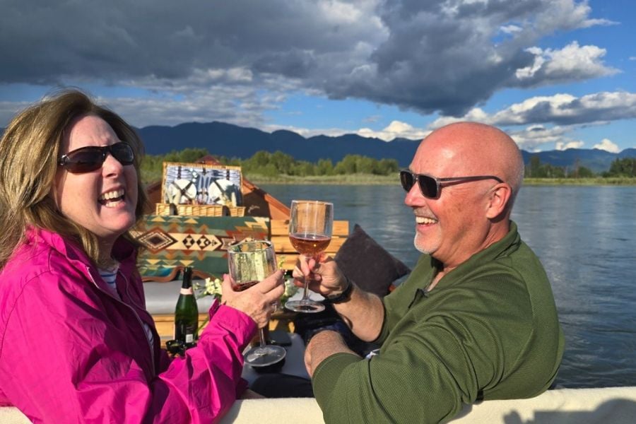 Couple laughing and clinking glasses on a peaceful boat ride.