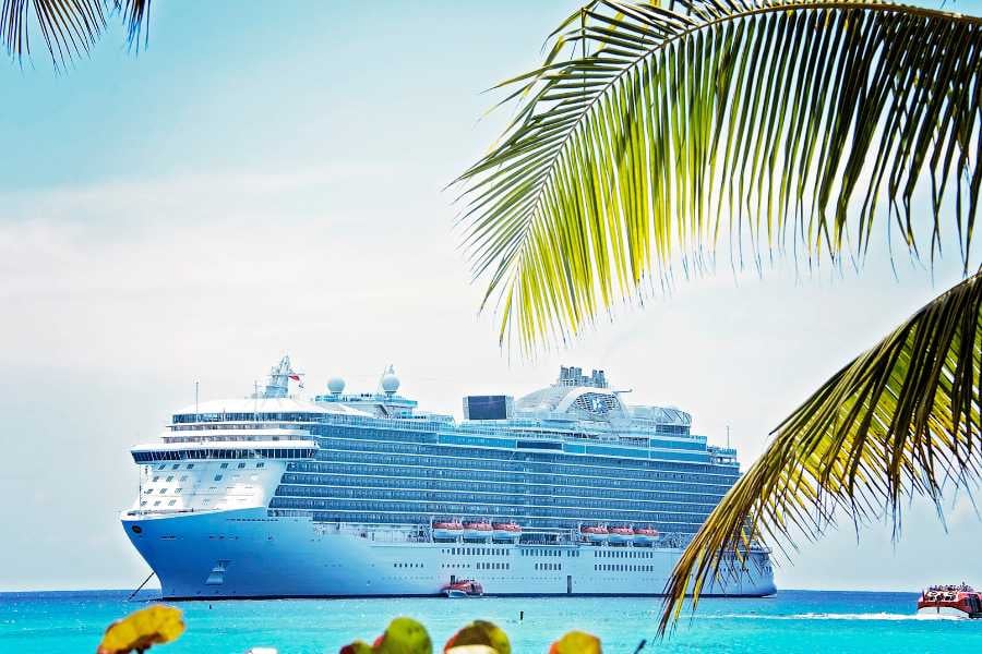 A massive cruise ship docked near palm trees, with clear skies and a vibrant beach view.