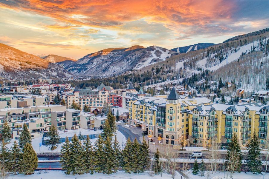The snow-covered mountain town of Vail glows beautifully beneath a vibrant sunset sky.