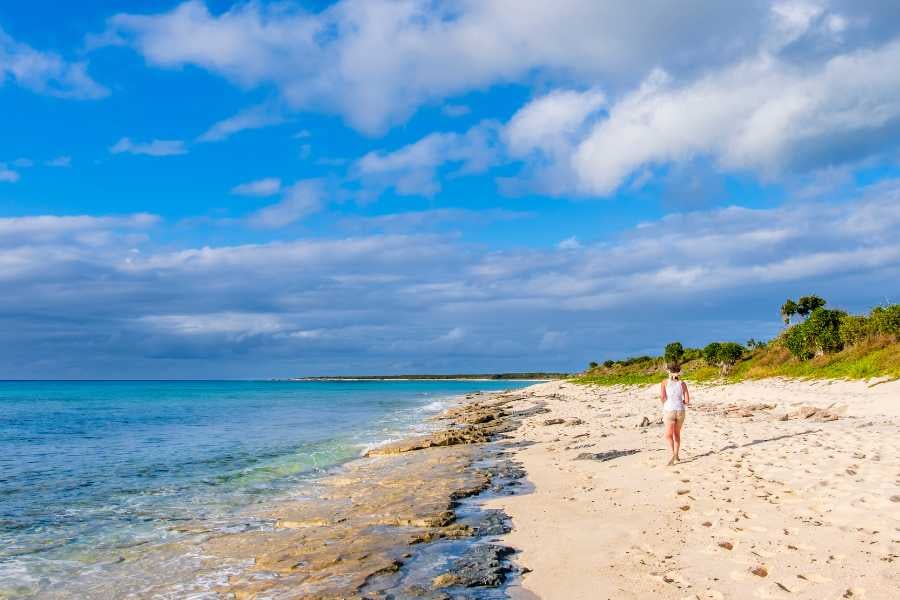 A bright, tropical beach with clear blue water and some rocks by the shore.