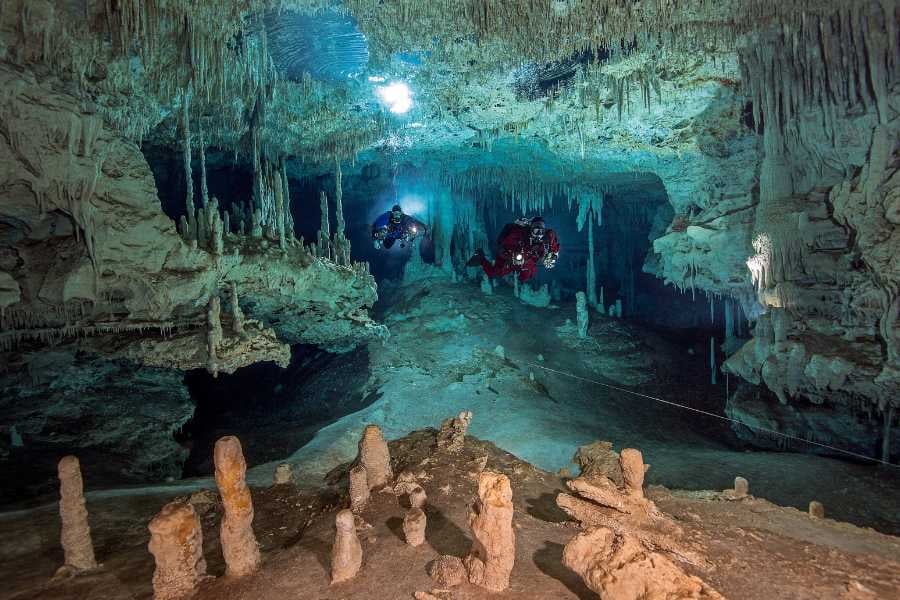 Two divers explore a magical underwater cave filled with intricate formations and a glowing, mysterious ambiance.